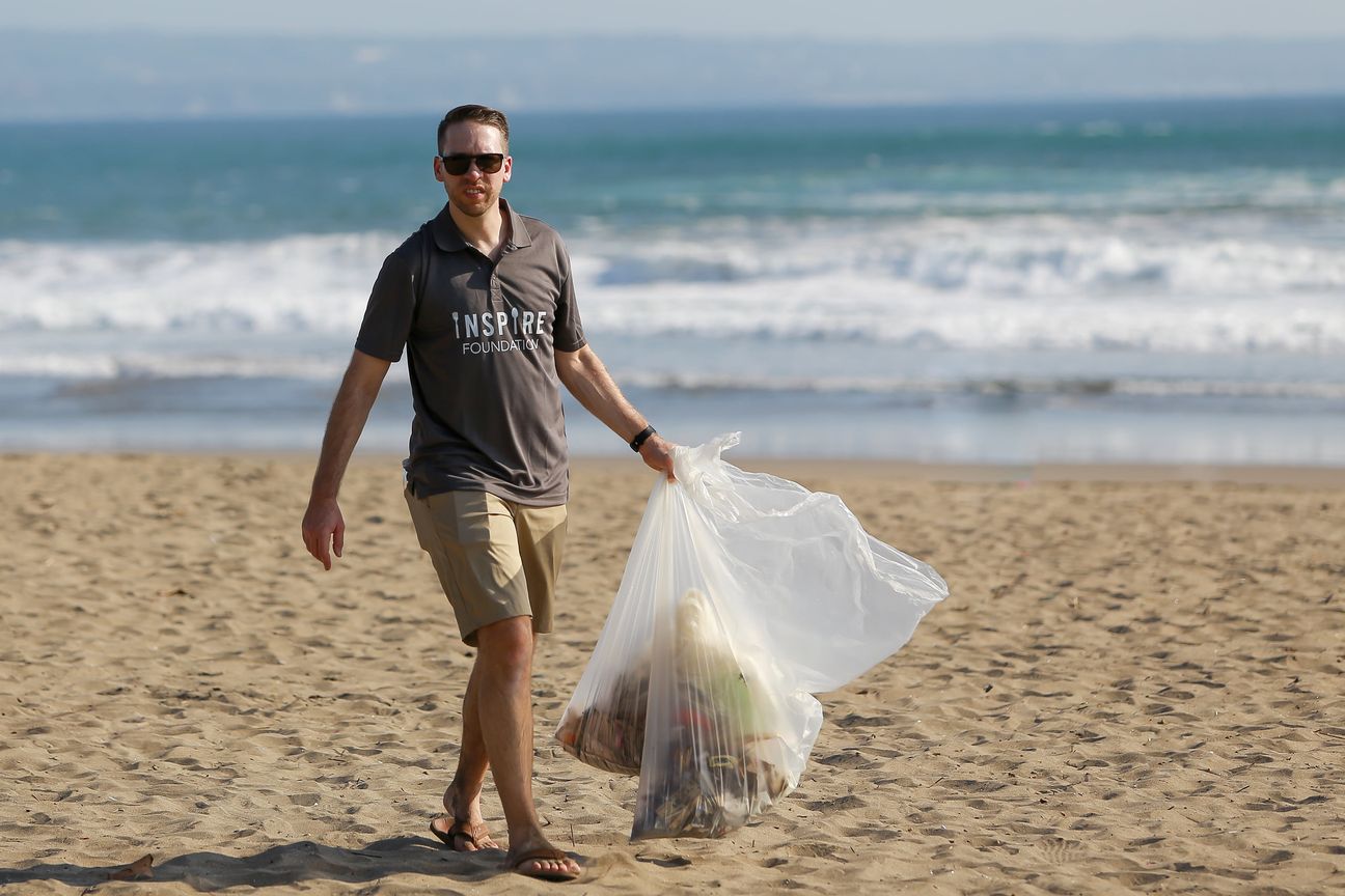 A volunteer carries a full sack of litter up the beach, surf breaking behind him
