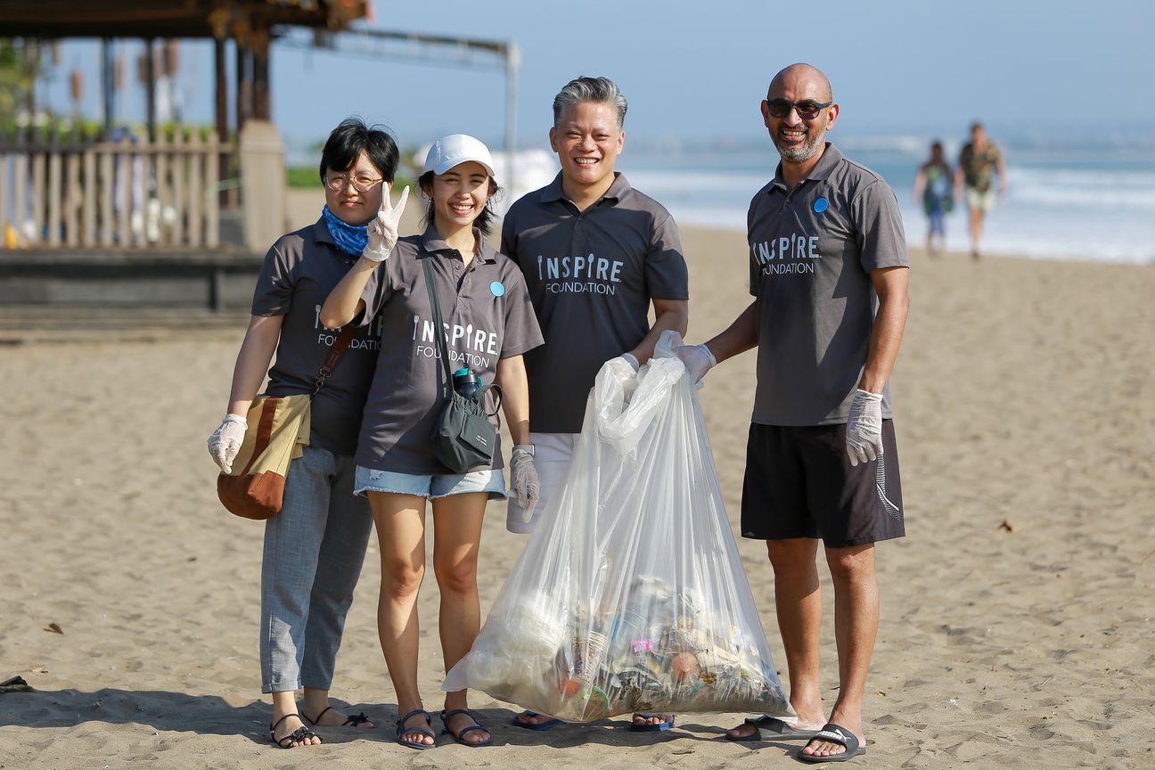Four volunteers stand around a full bag of collected litter on the sand
