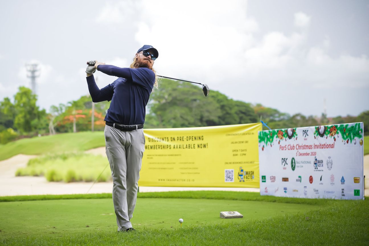 A golfer follows through on the tee in front of the tournament boards
