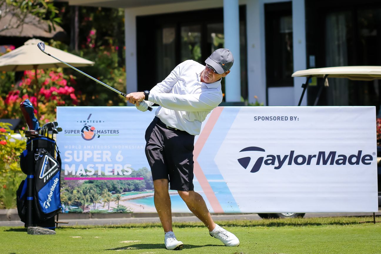 A golfer completes a swing beside a tournament sponsor board