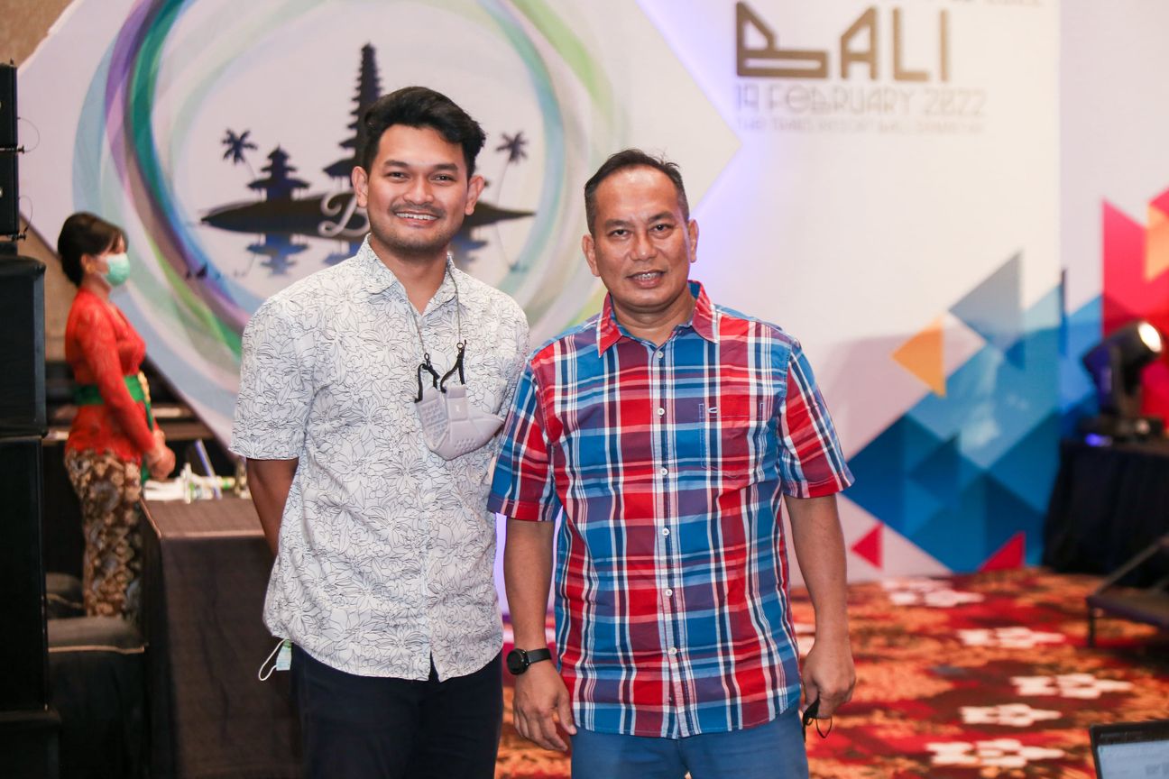 Two men stand arm in arm in front of the backdrop at the end of the day