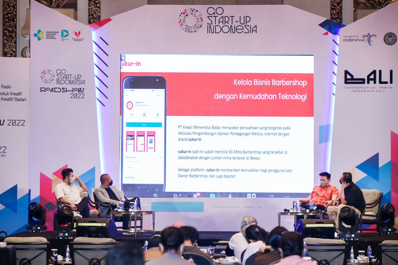 Four panellists on stage either side of a slide showing a barbershop booking app