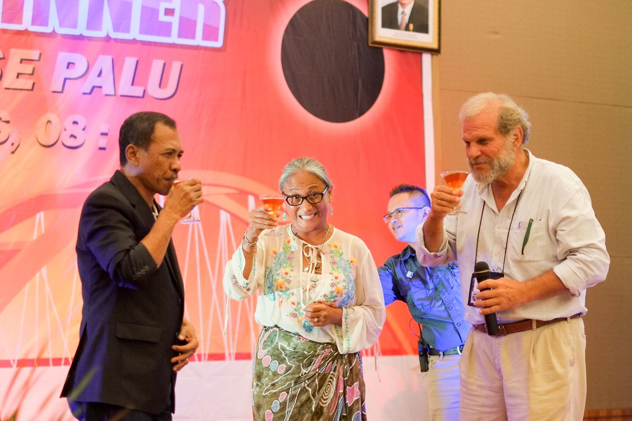 Guests drink and laugh on stage, one of them still holding the microphone