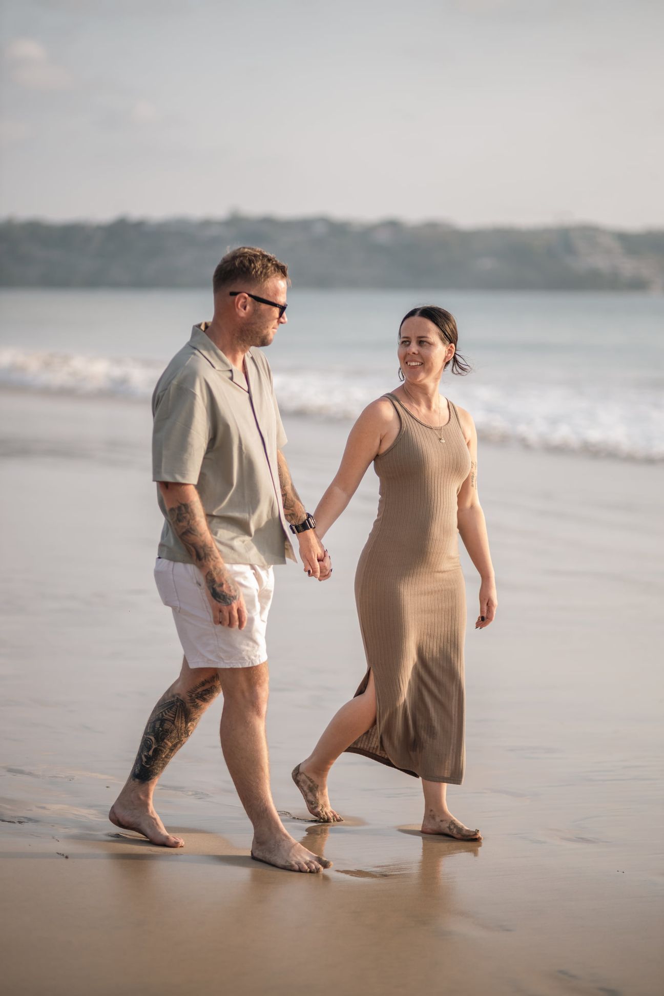 Two adults walk hand in hand along the waterline