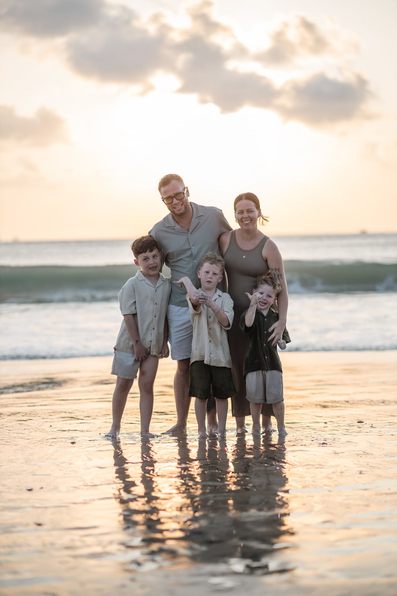 A family stand together in shallow water under warm evening light