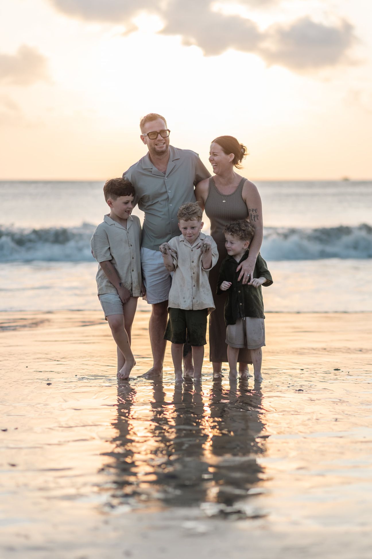 A family stand together in shallow water under warm evening light