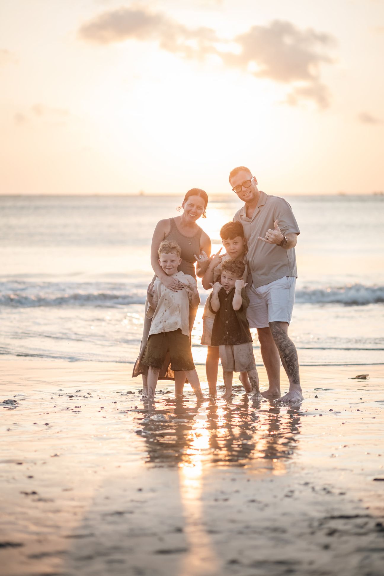 A family stand together in shallow water under warm evening light