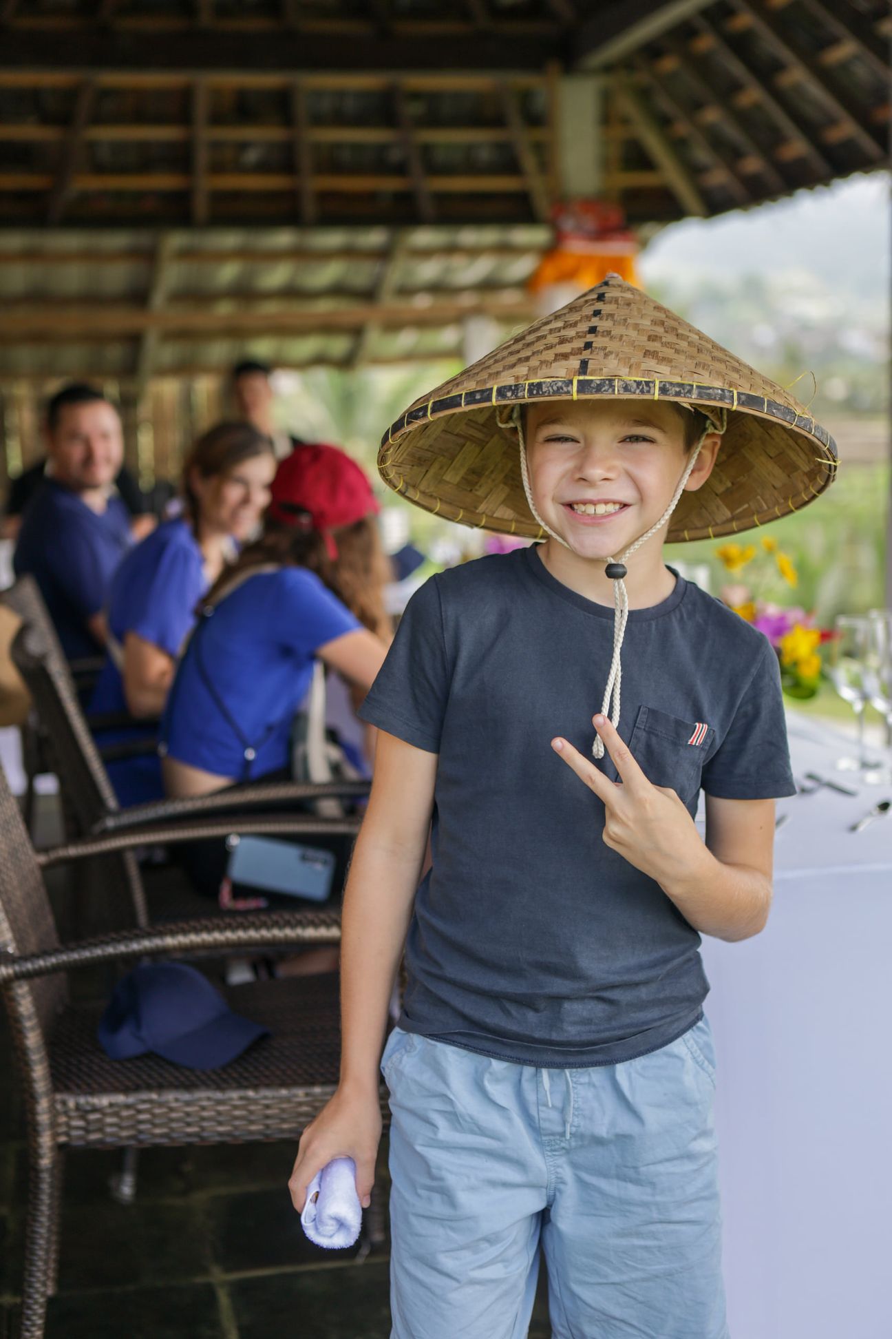 A boy in a woven conical hat flashes a peace sign beside the lunch table