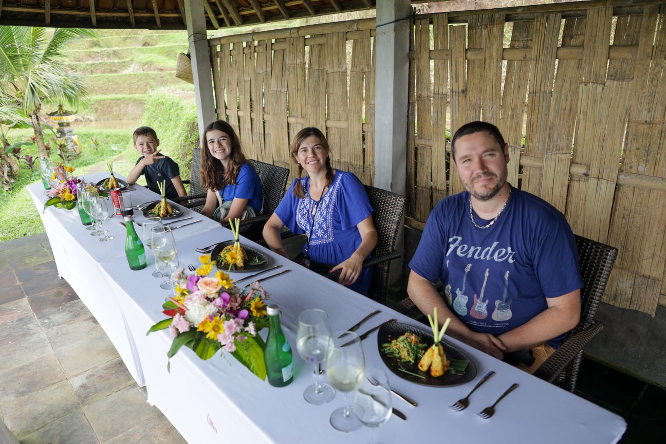 A family of four smile from a dining table overlooking green rice terraces