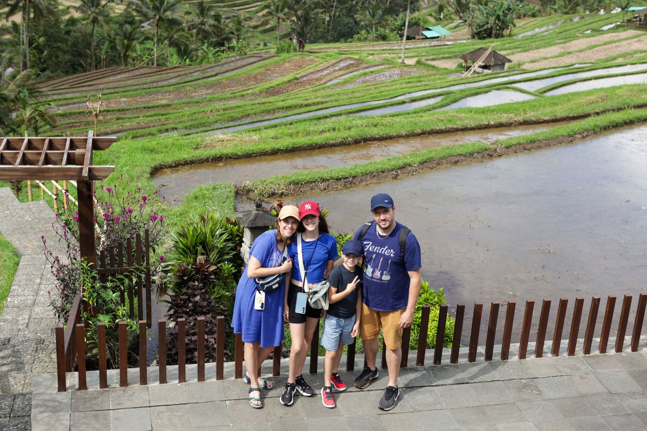 A family of four smile from a dining table overlooking green rice terraces