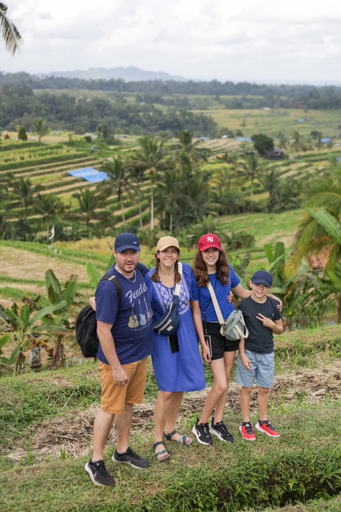 A family of four in matching blue shirts pose on a grassy bank among the rice terraces
