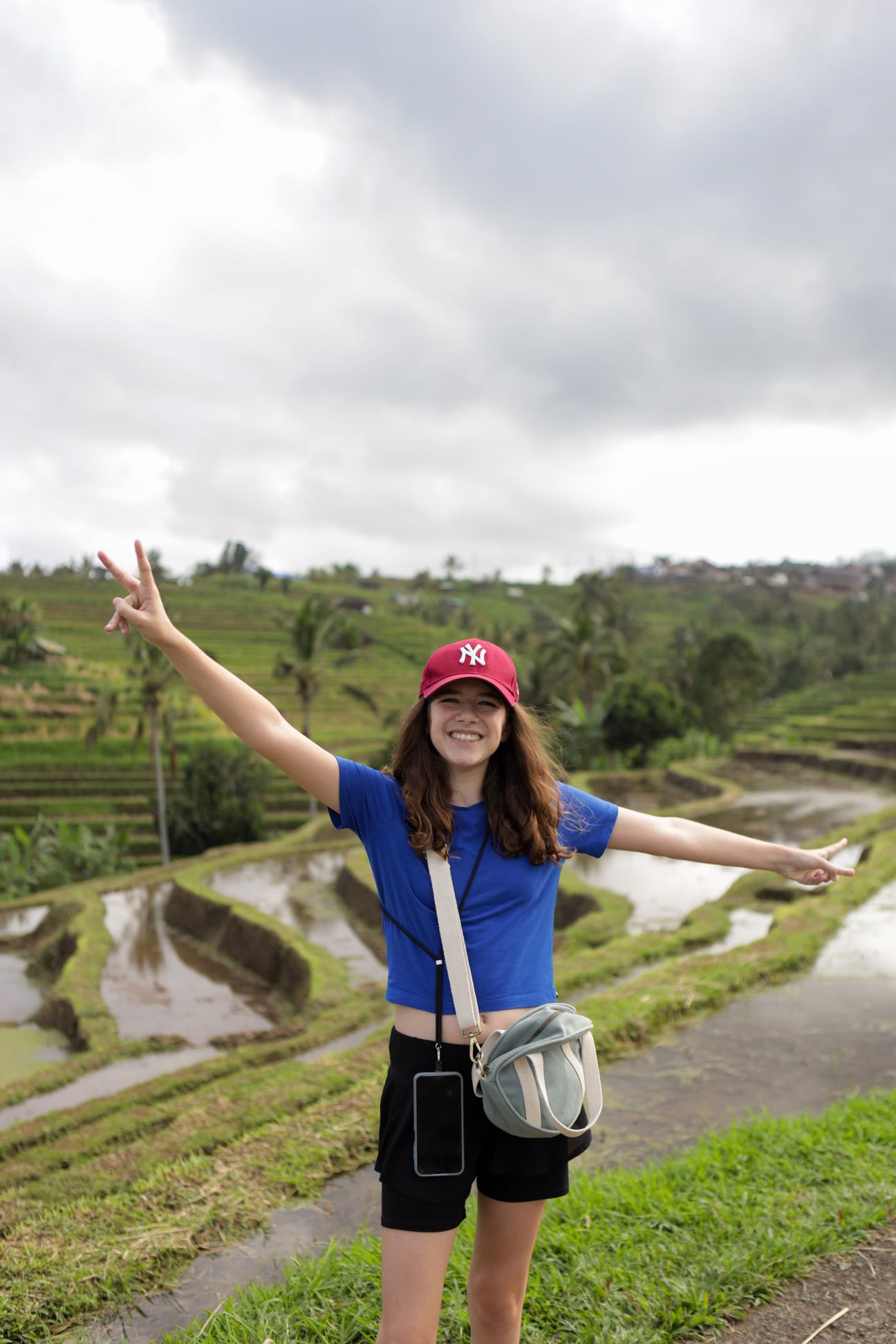 A girl in a red cap throws her arms wide on a path through the rice terraces