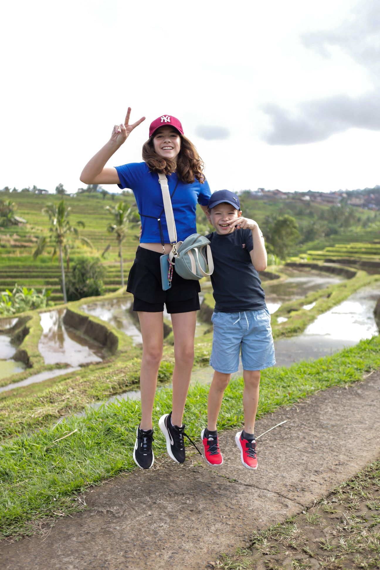 A sister and brother leap into the air on a path through the rice terraces