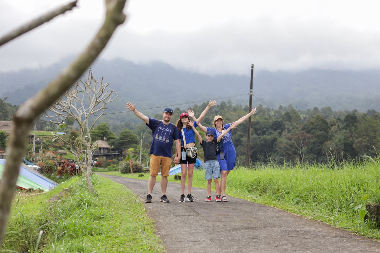 A family of four smile from a dining table overlooking green rice terraces