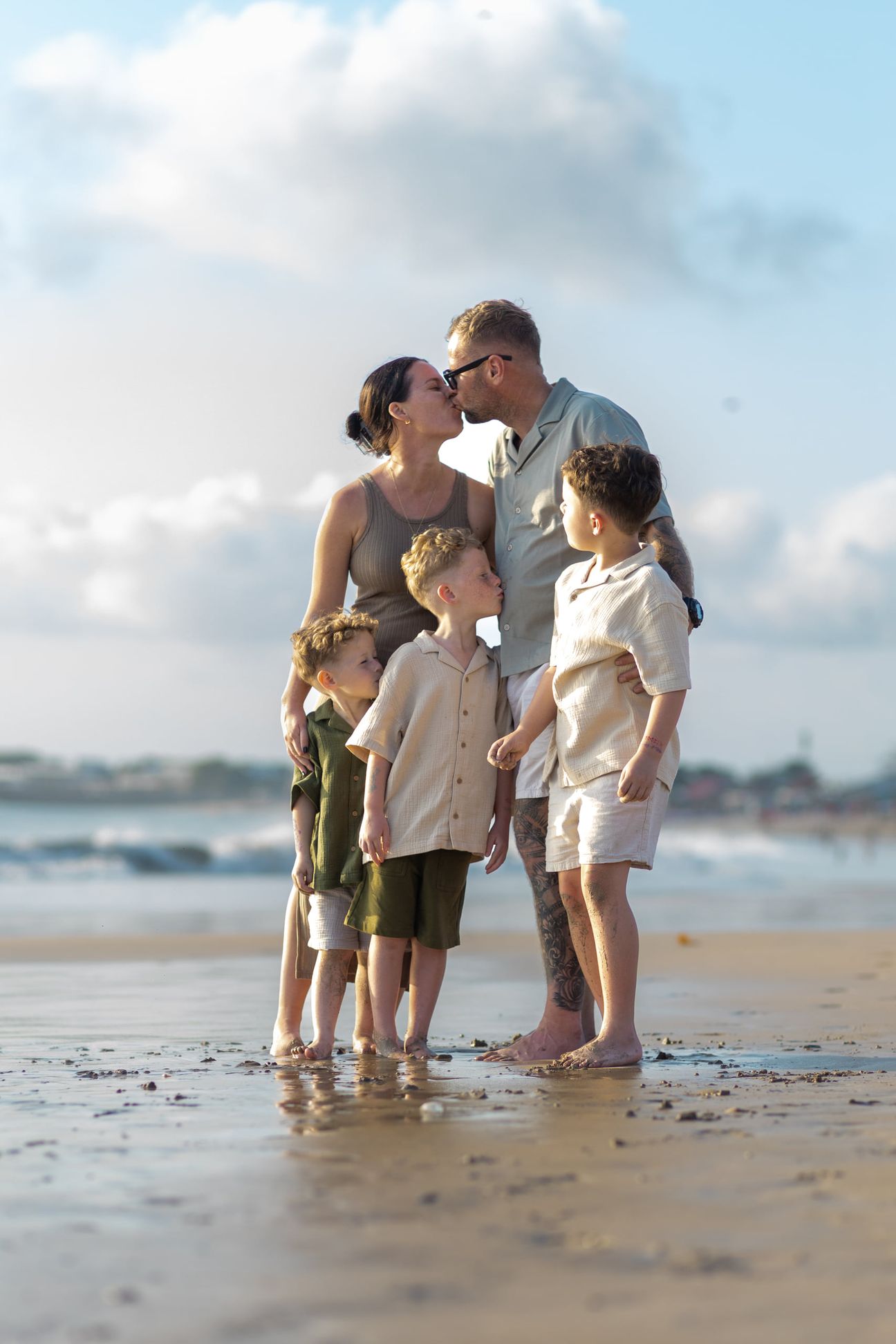 A family stand together in shallow water under warm evening light