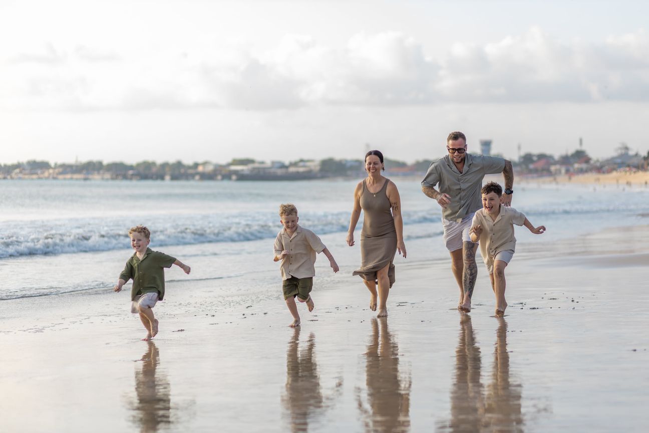 A family run together across wet sand beside the sea