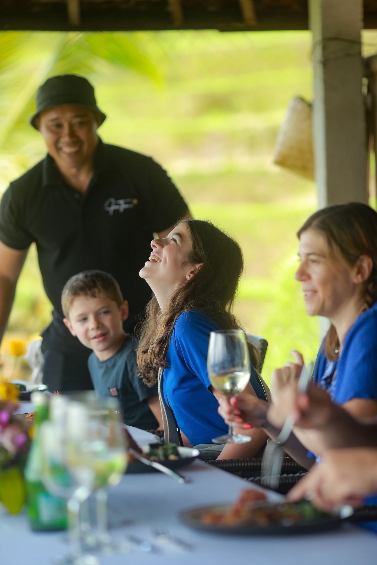 A smiling guide leans in beside a family at a lunch table in the rice fields
