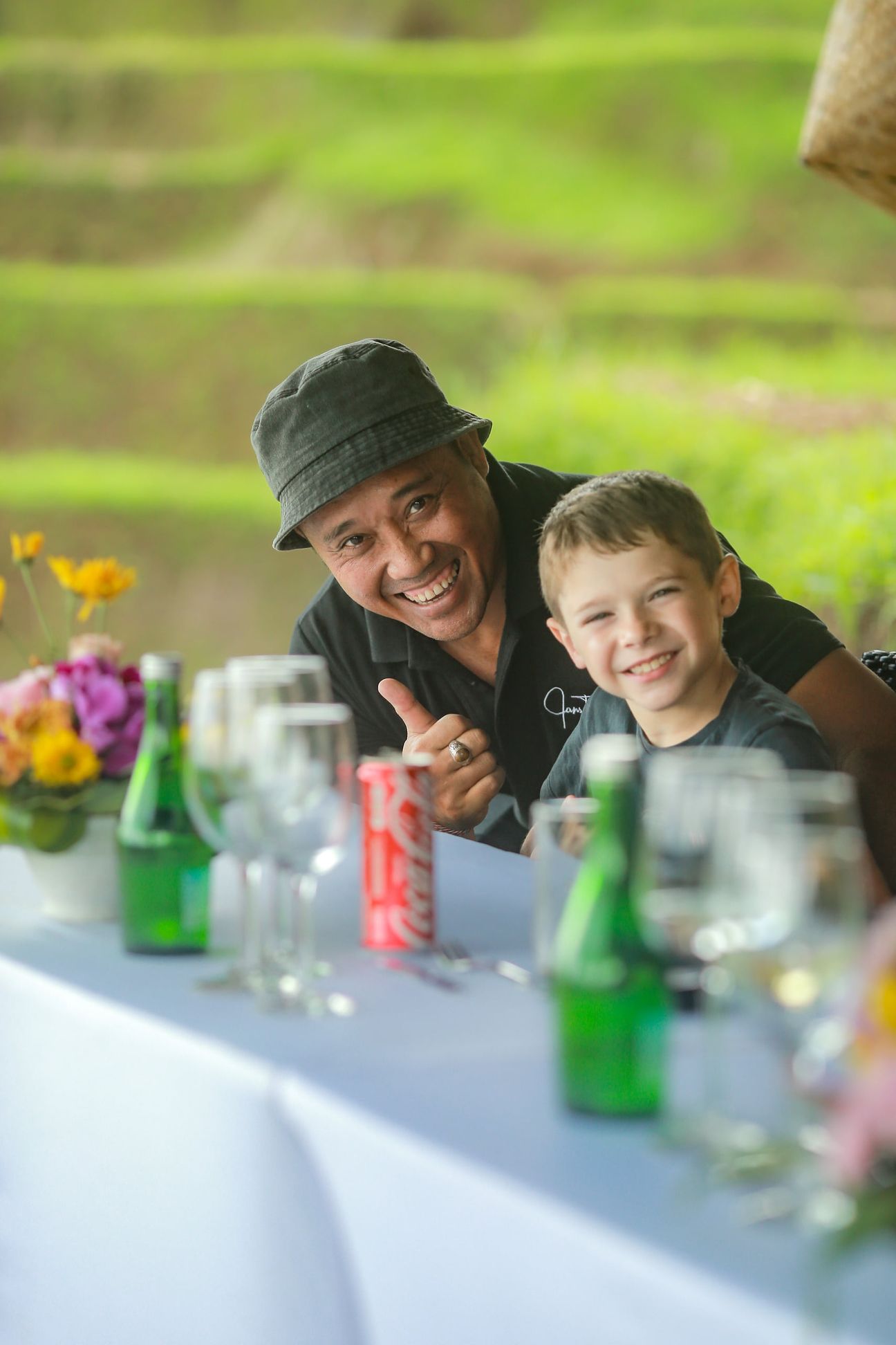 A smiling guide leans in beside a family at a lunch table in the rice fields
