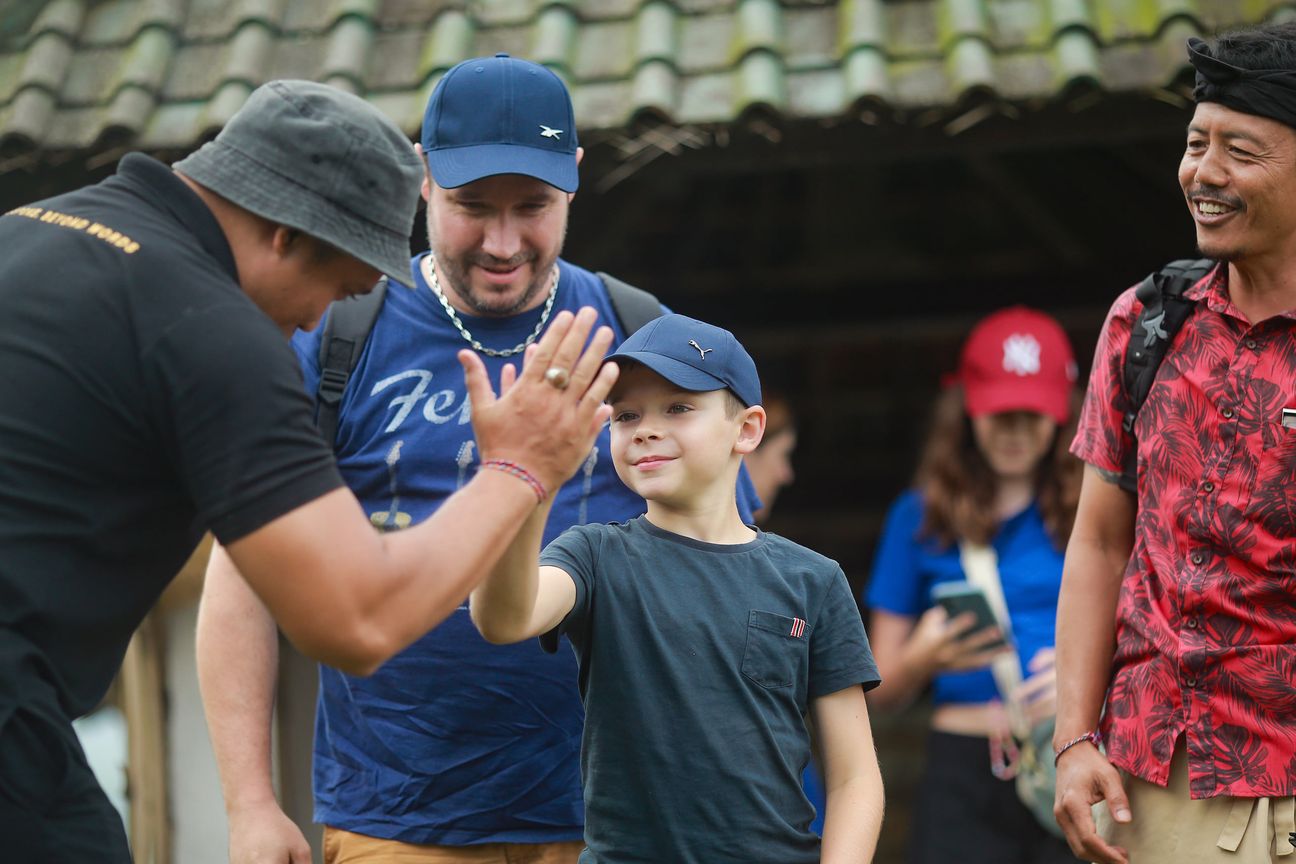 A guide high-fives a boy in a blue cap as his family look on