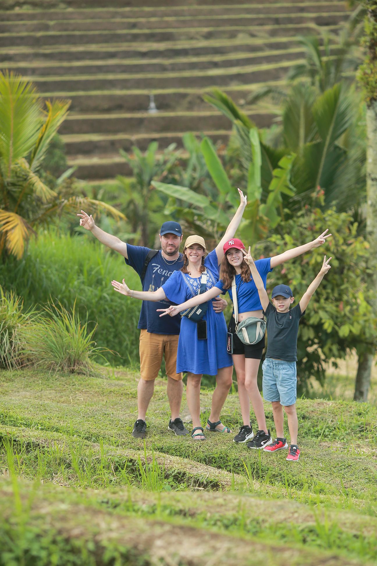A family of four in matching blue shirts pose on a grassy bank among the rice terraces