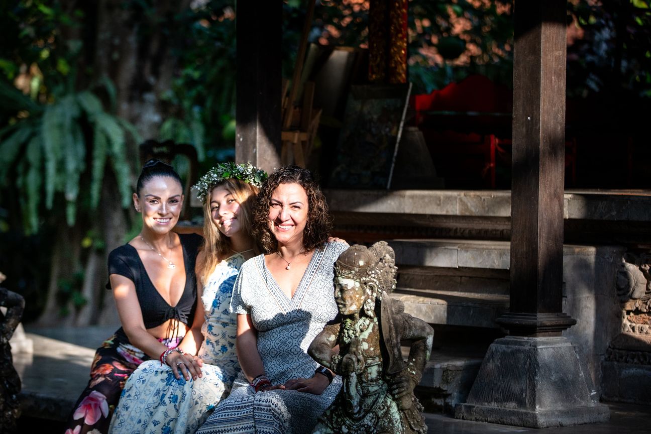 A mother and her adult daughters share a relaxed portrait in a garden