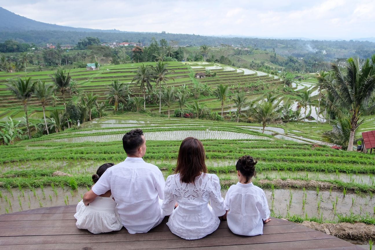 A family of four dressed in white sit together looking across expansive green rice terraces