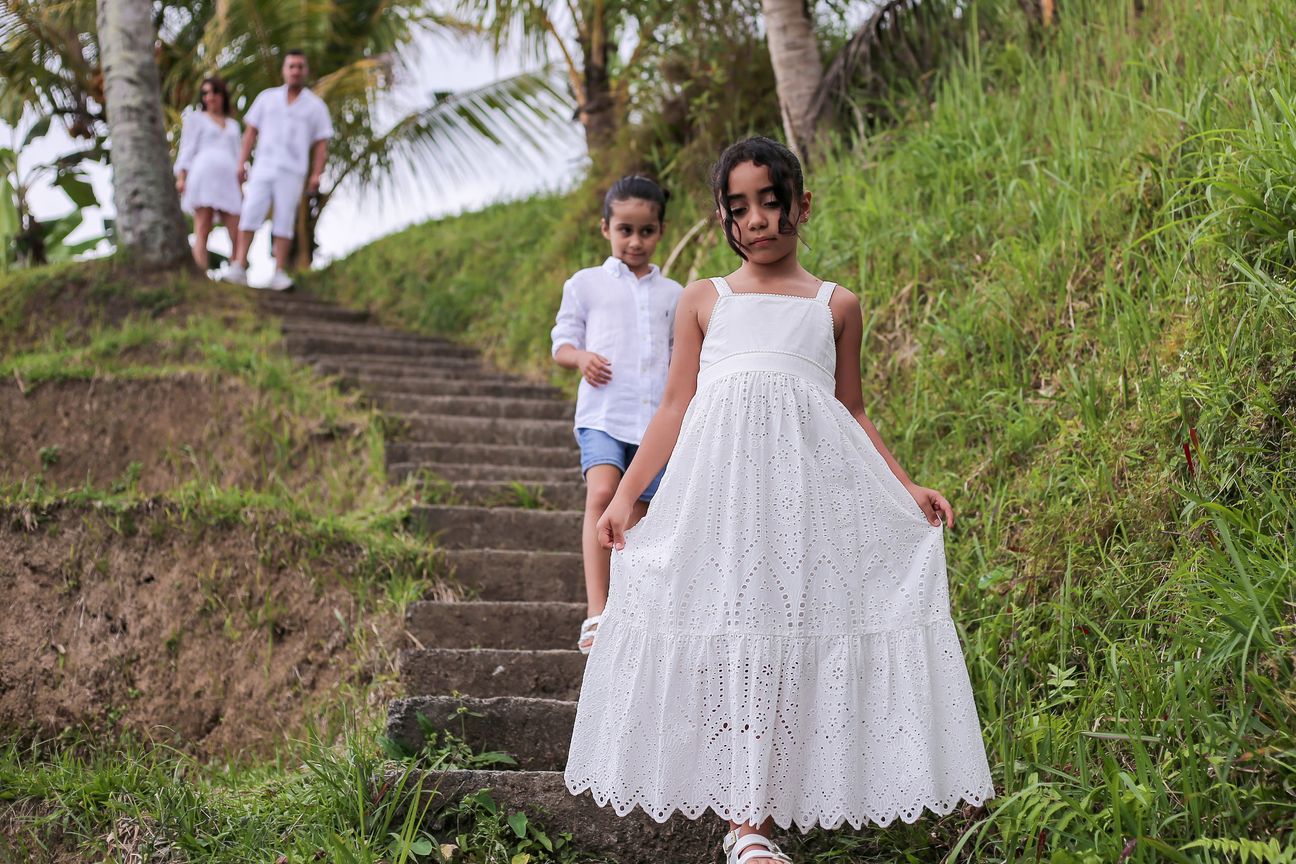A family dressed in white make their way down stone steps through a garden