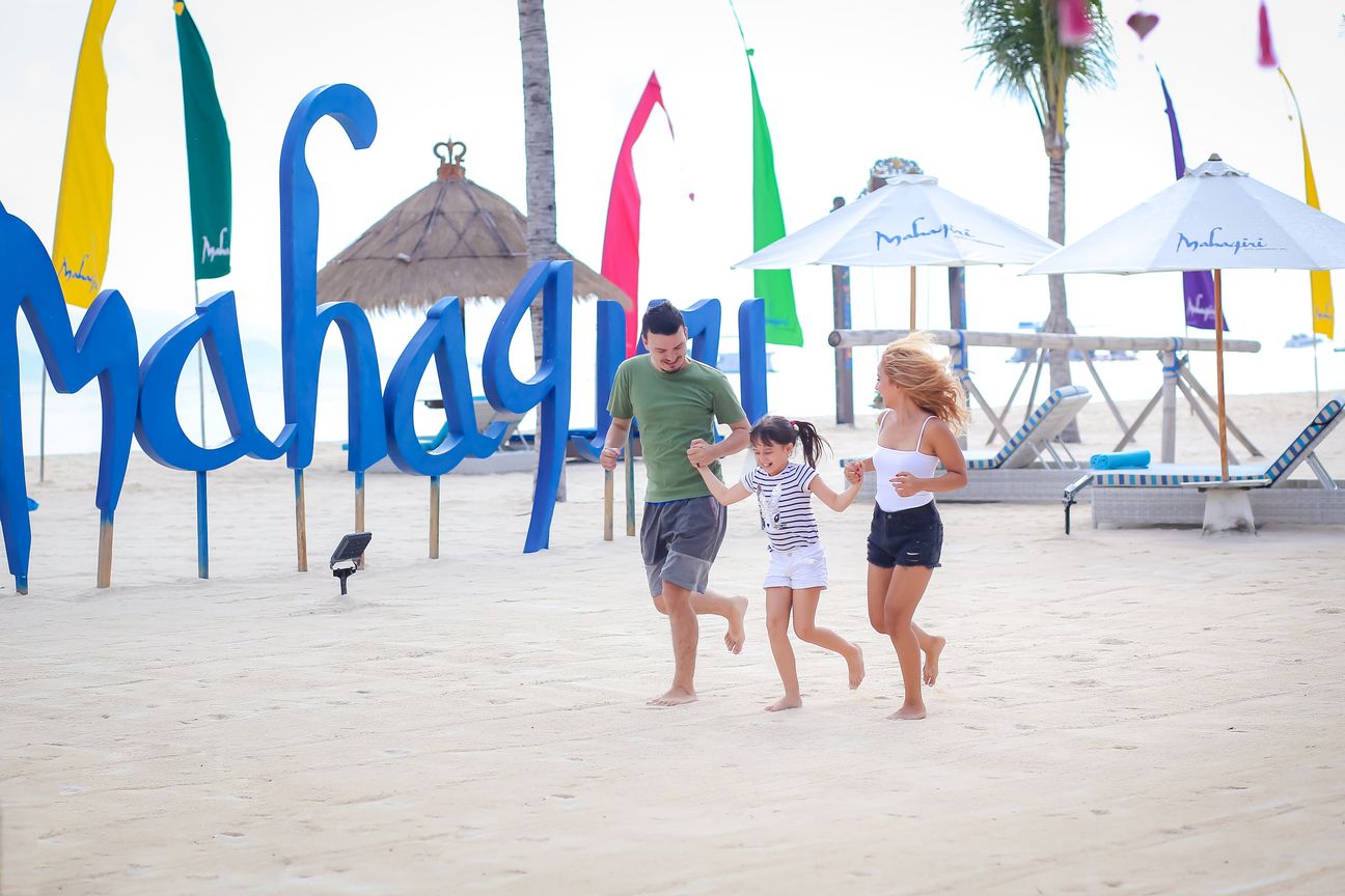 Three travellers stand together beside a colourful Mahagiri sign
