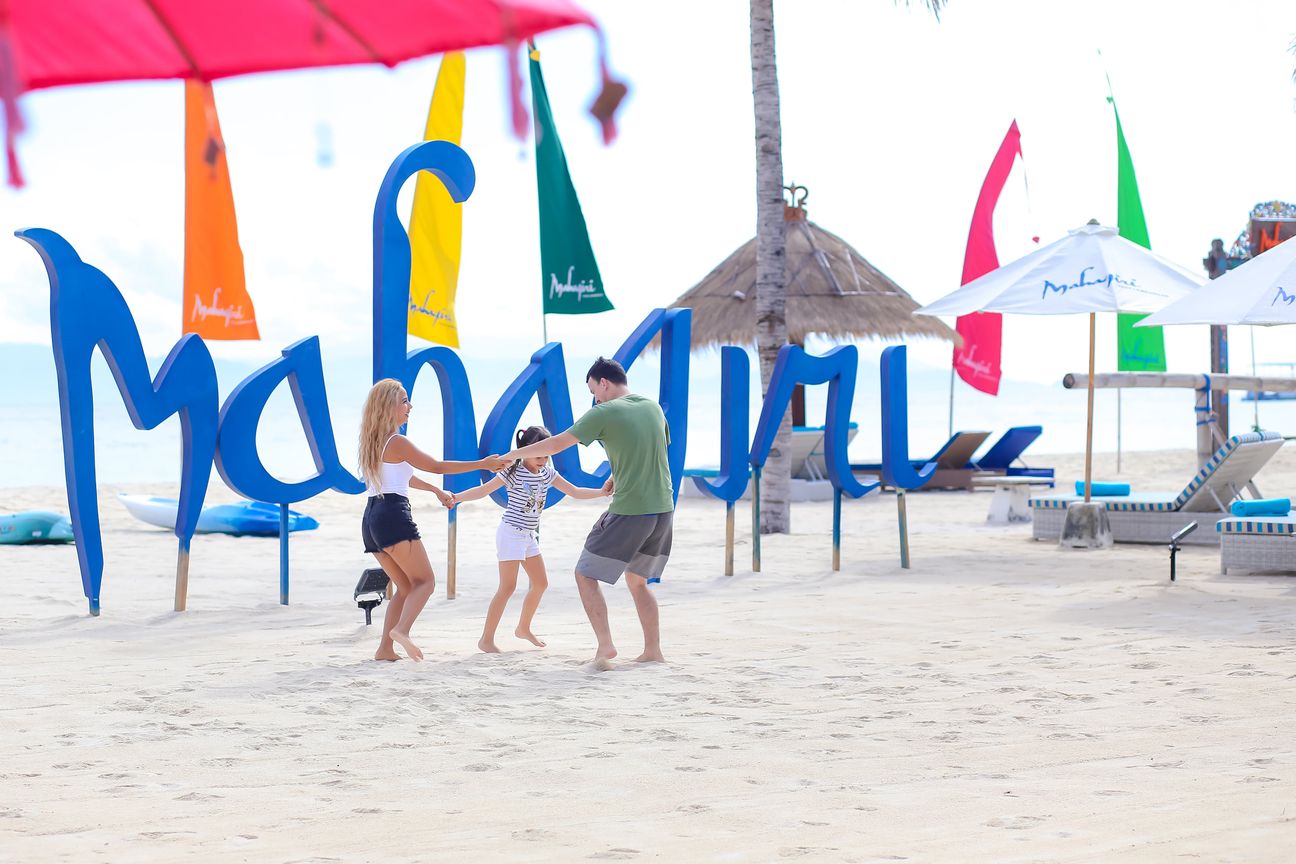Three travellers stand together beside a colourful Mahagiri sign