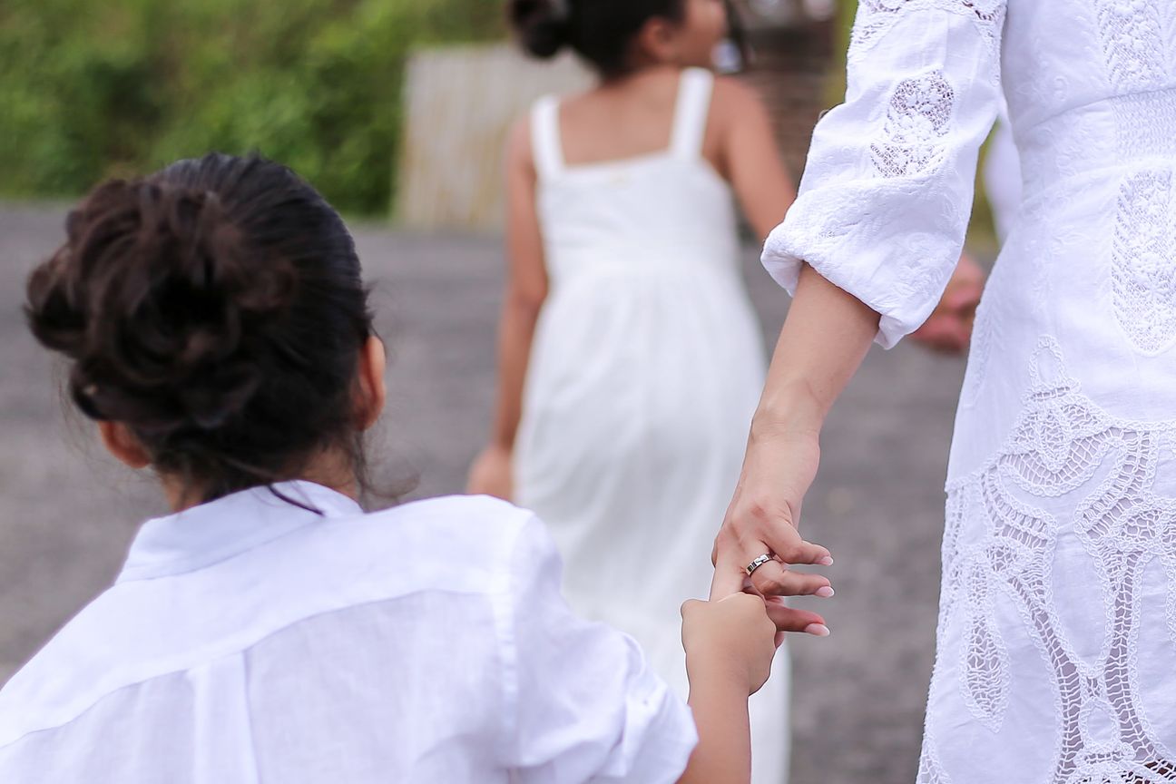 Two girls in white dresses hold their parents’ hands on the terrace path