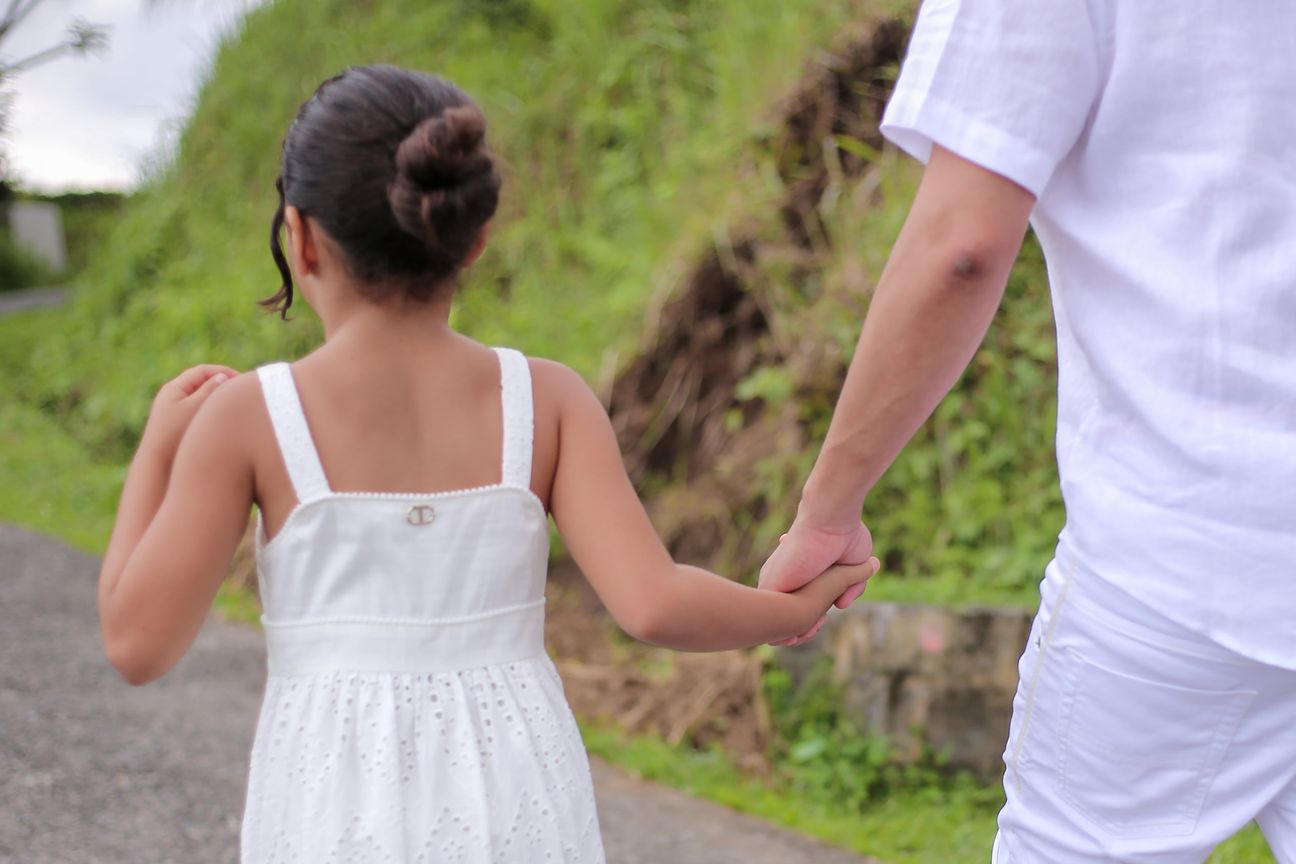 Two girls in white dresses hold their parents’ hands on the terrace path