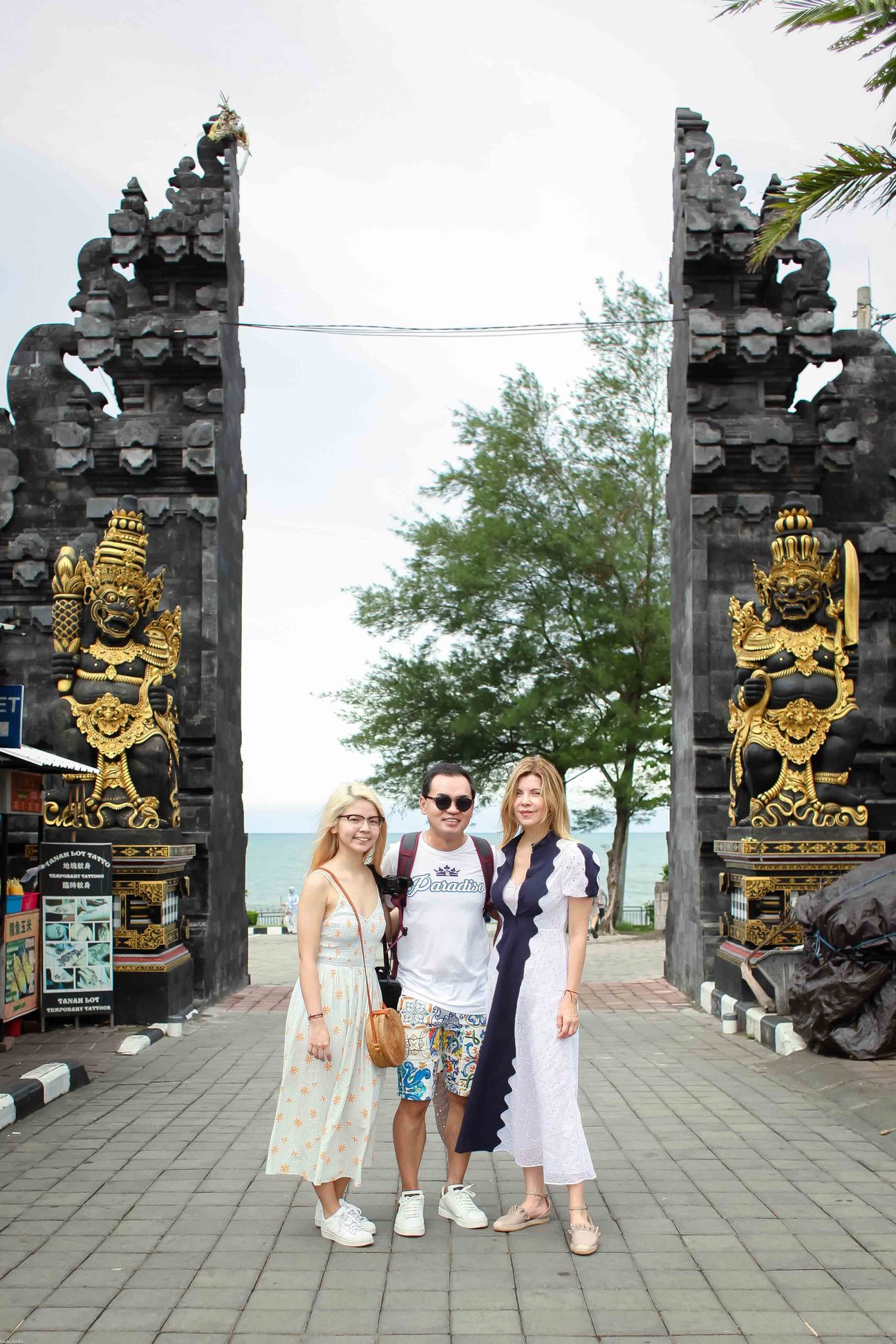 Three travellers pose together at a temple and coastal viewpoint in Bali