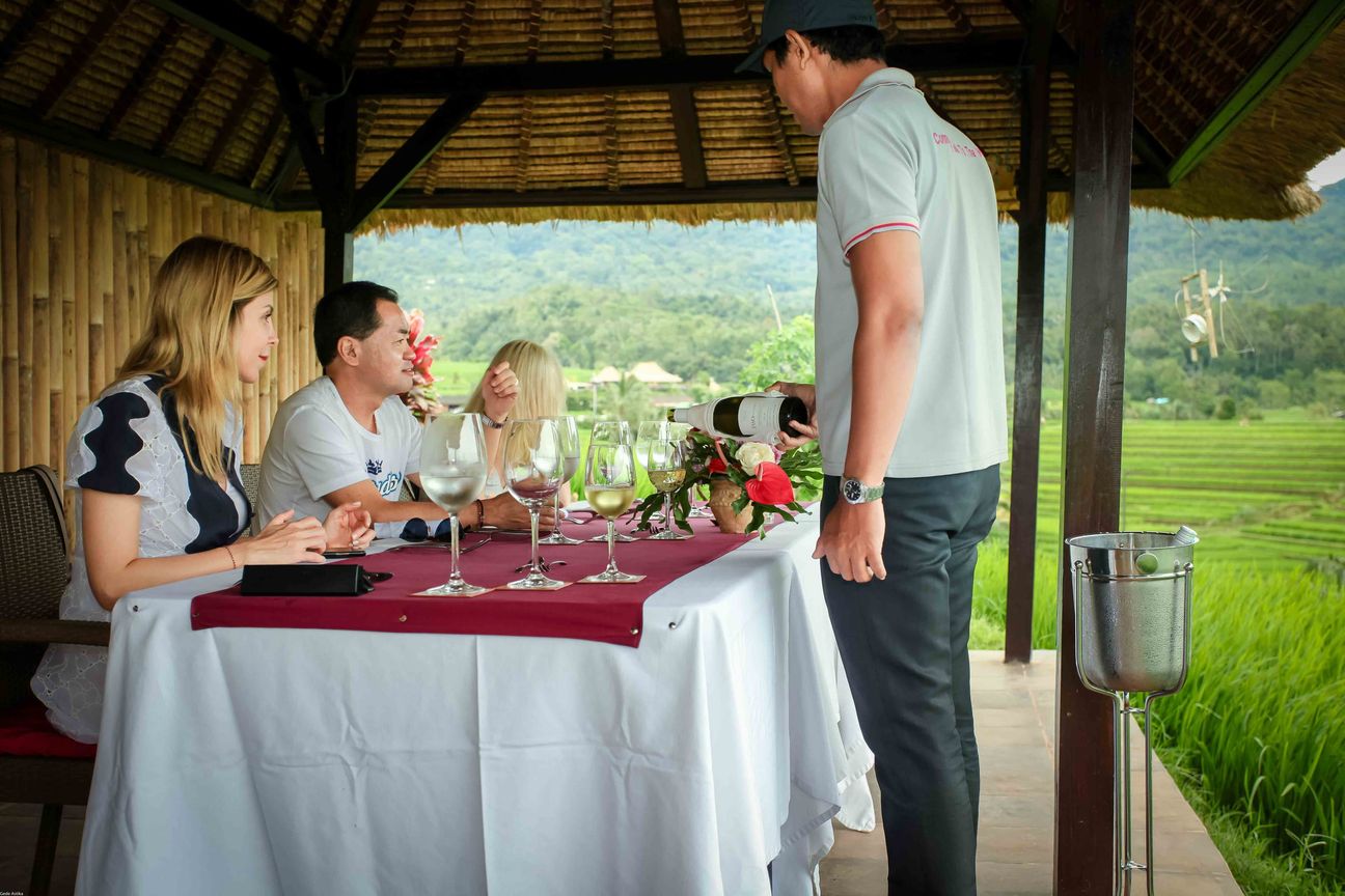 Guests share a meal in an open pavilion overlooking rice fields