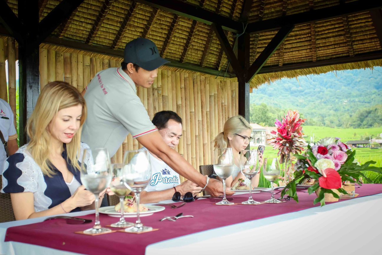 Guests share a meal in an open pavilion overlooking rice fields