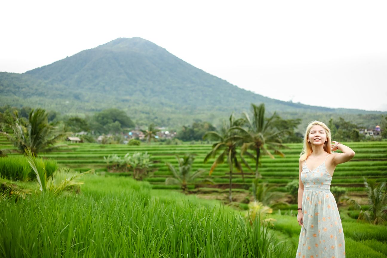 A traveller poses among vivid green rice terraces with mountains behind