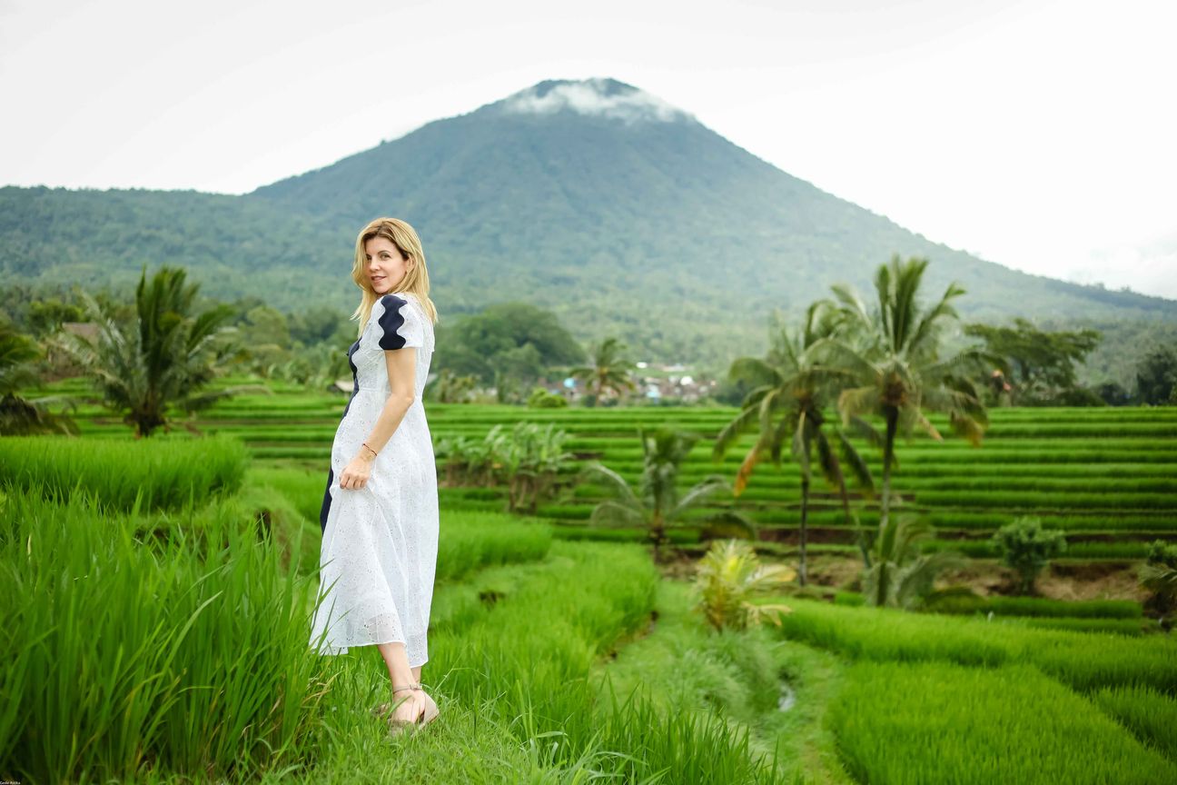 A traveller poses among vivid green rice terraces with mountains behind