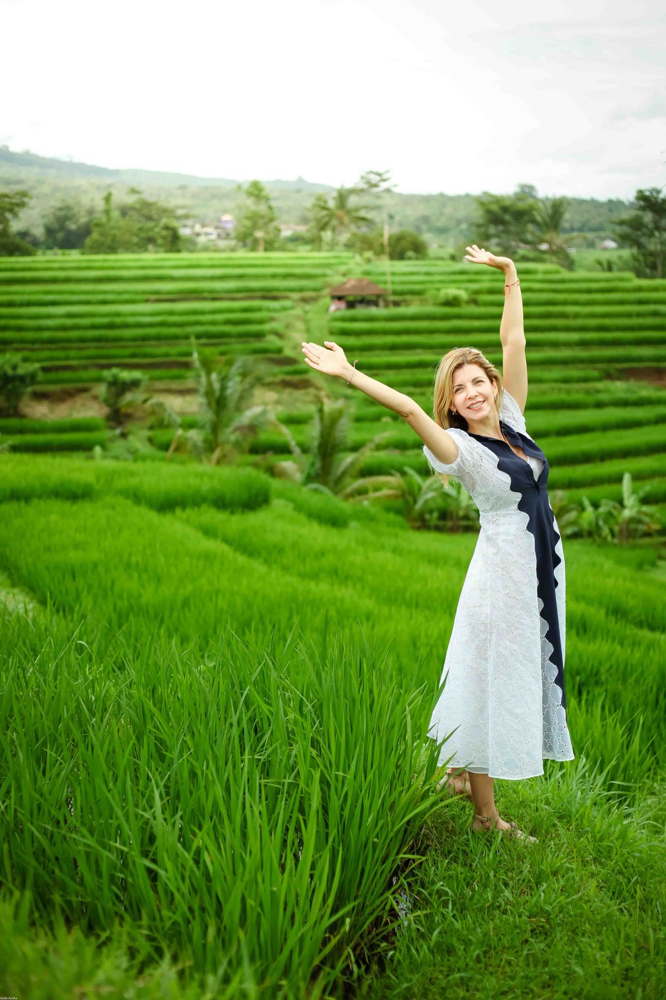 A traveller poses among vivid green rice terraces with mountains behind