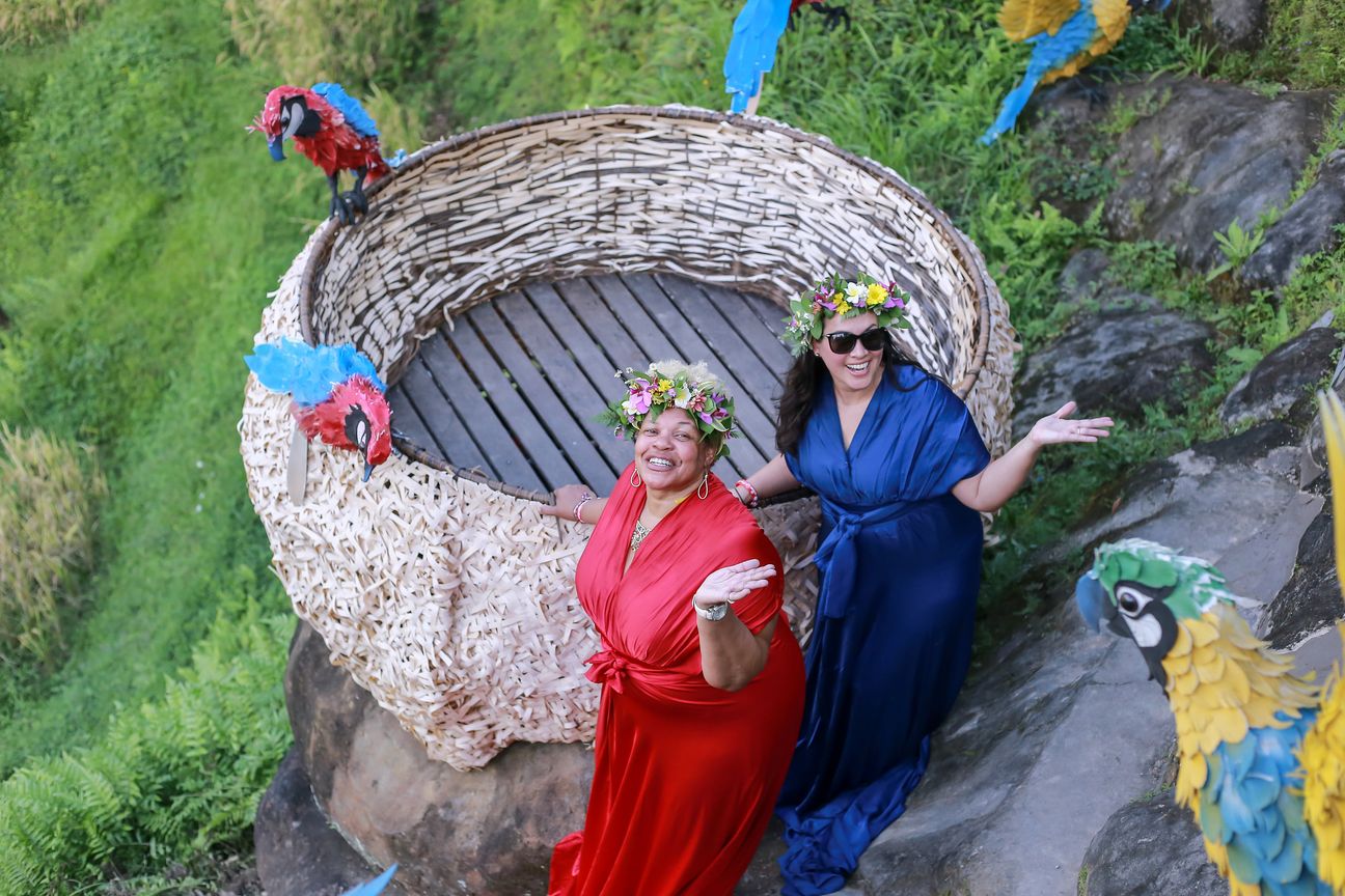Two women in long red and blue gowns pose together in a woven photo frame
