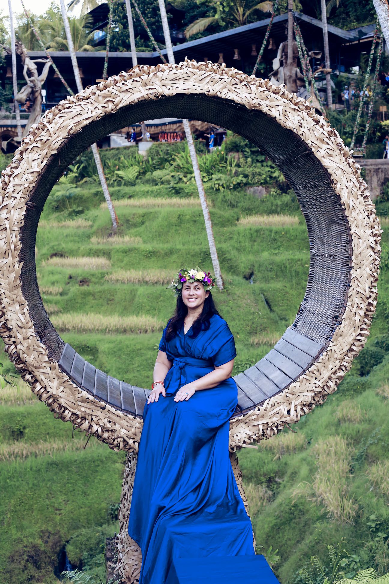 A woman in a long gown sits inside a woven ring above the rice terraces