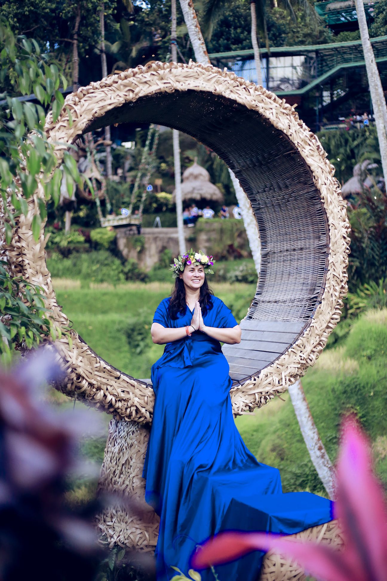 A woman in a long gown sits inside a woven ring above the rice terraces