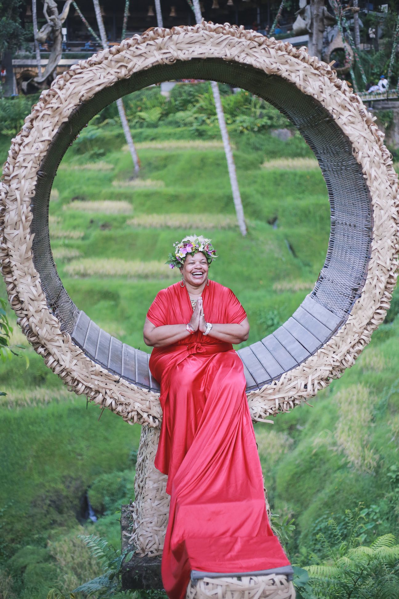 A woman in a long gown sits inside a woven ring above the rice terraces