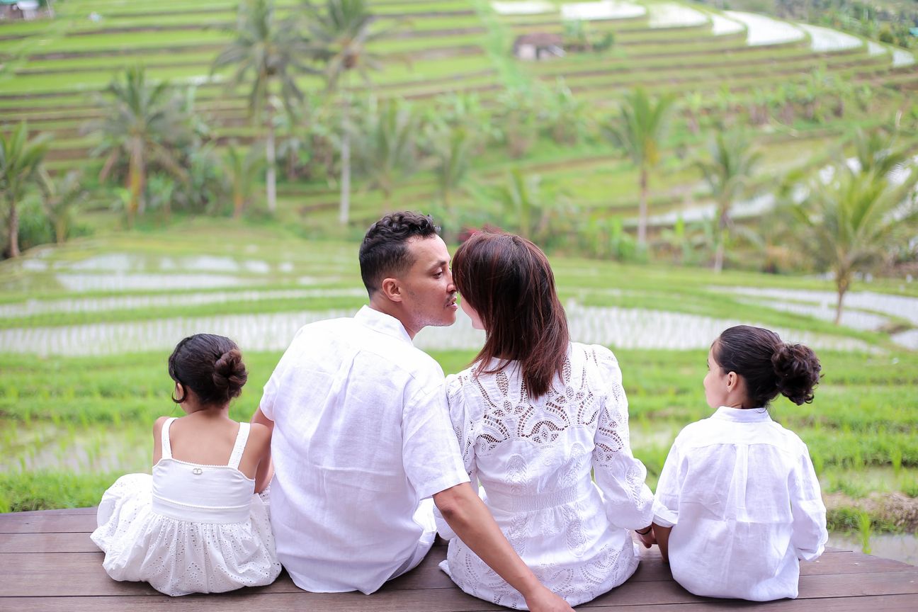 A family of four sit together on a stone terrace with hills and rice paddies behind them