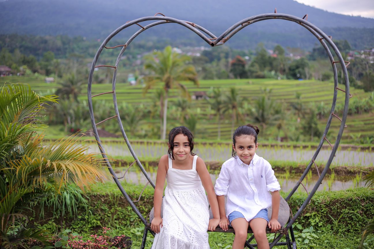A sister and brother sit inside a metal heart frame above the rice terraces