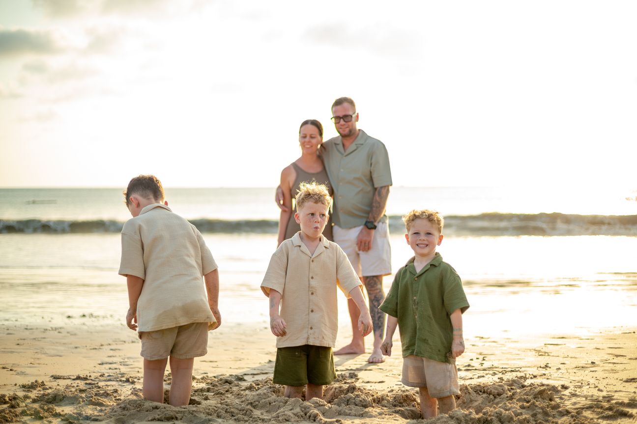 A family of five standing barefoot on wet sand in late afternoon light