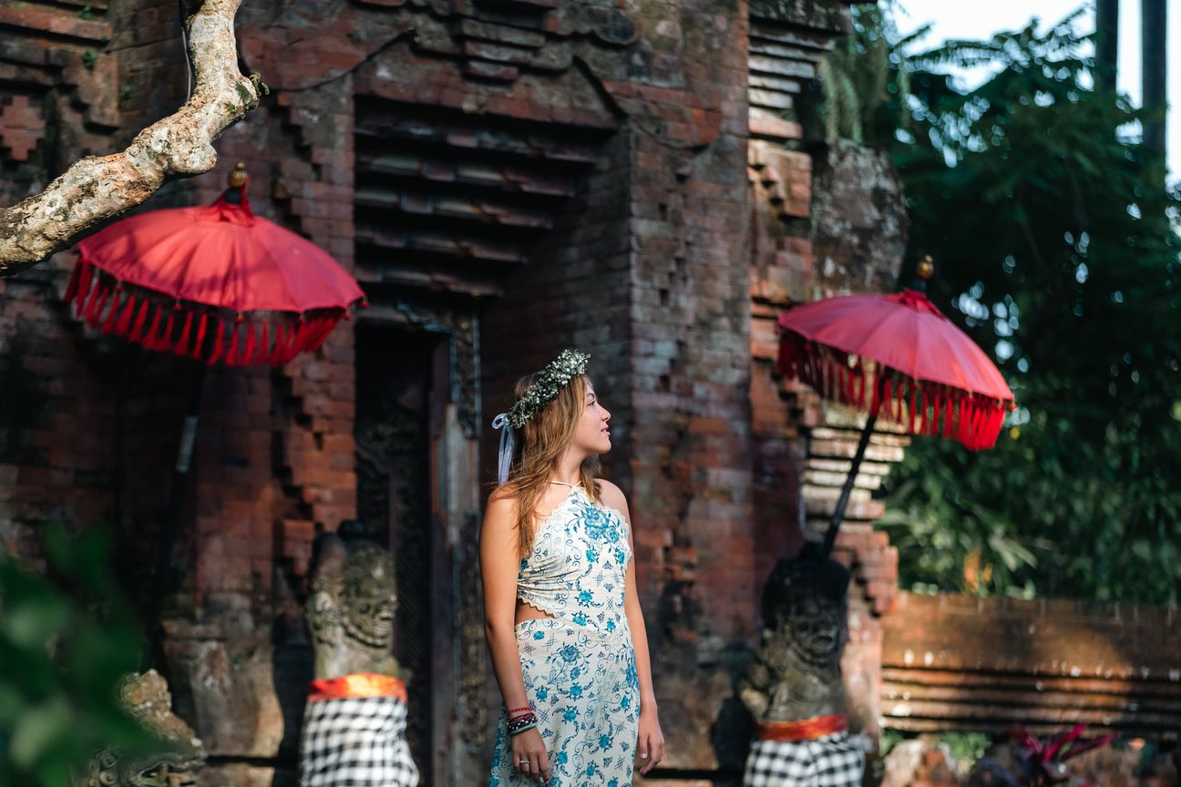 A woman in a floral dress poses in the shade of a tropical Balinese garden