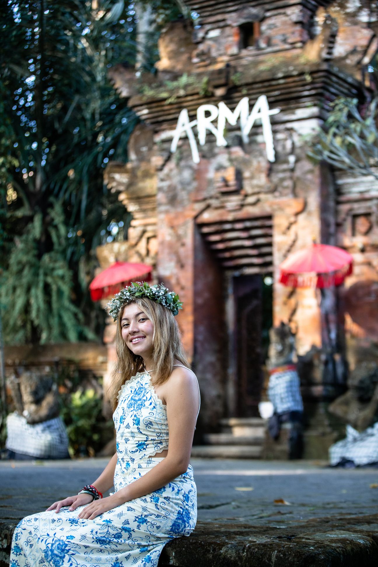 A woman in a floral dress poses in the shade of a tropical Balinese garden