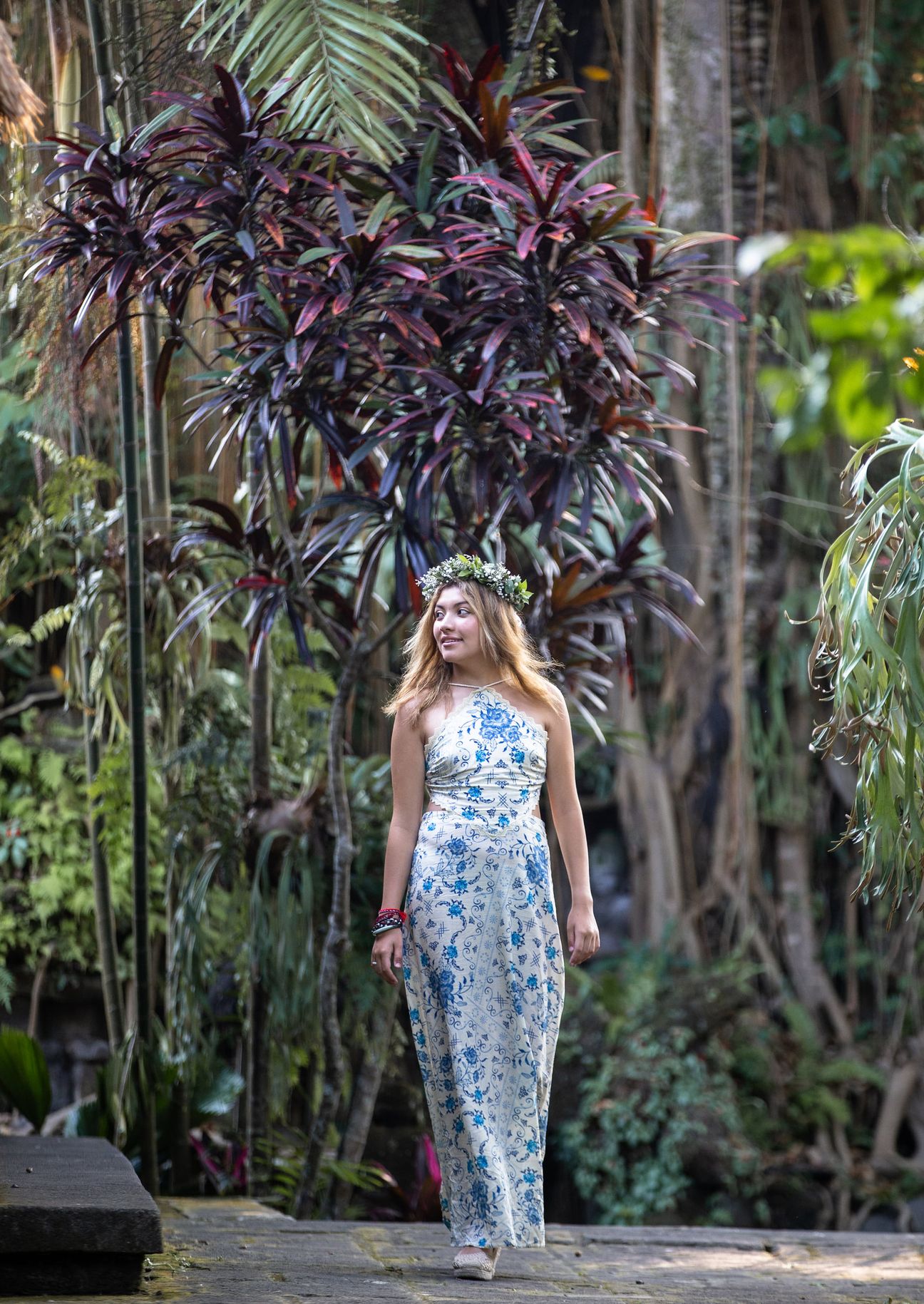 A woman in a floral dress poses in the shade of a tropical Balinese garden