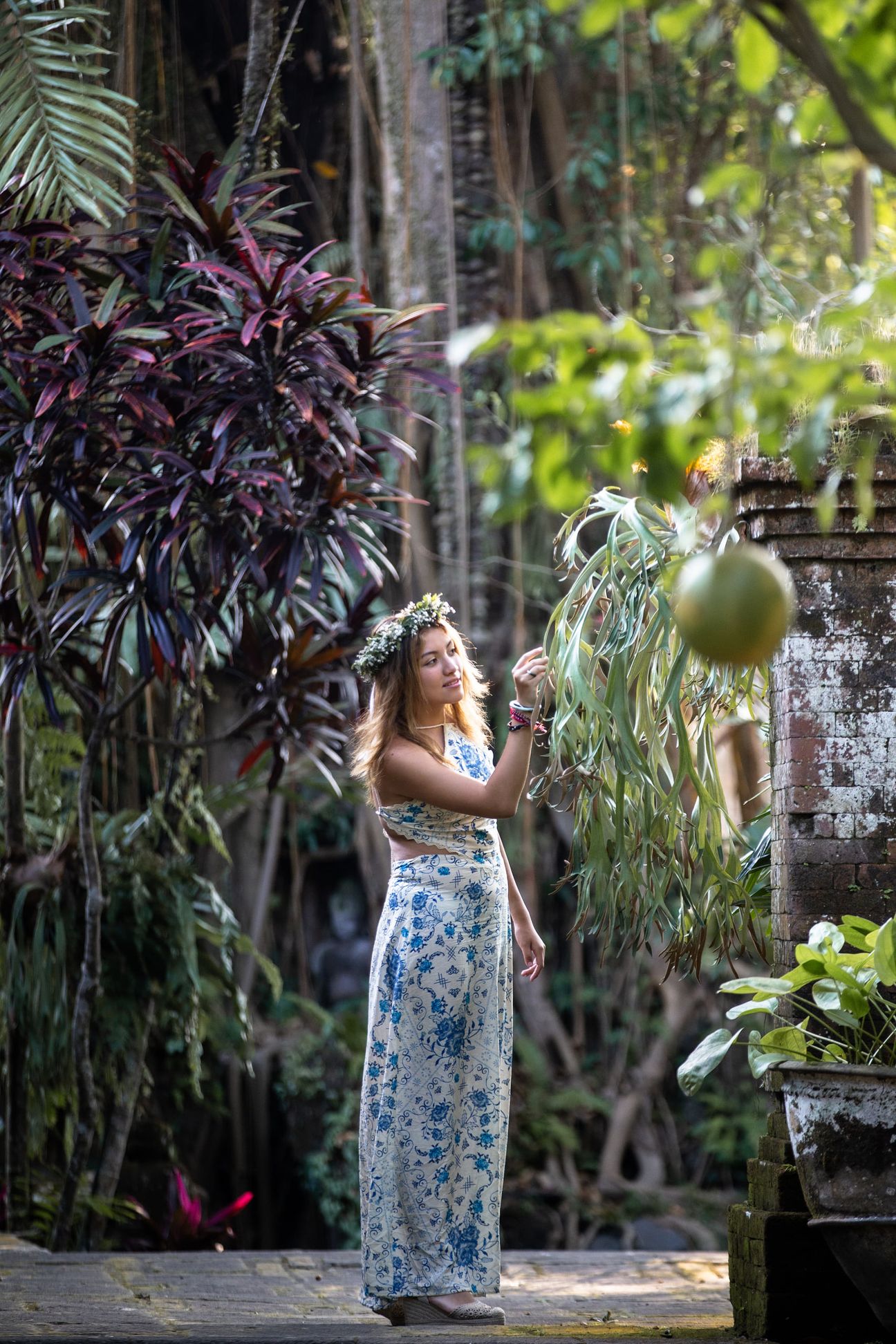 A woman in a floral dress poses in the shade of a tropical Balinese garden