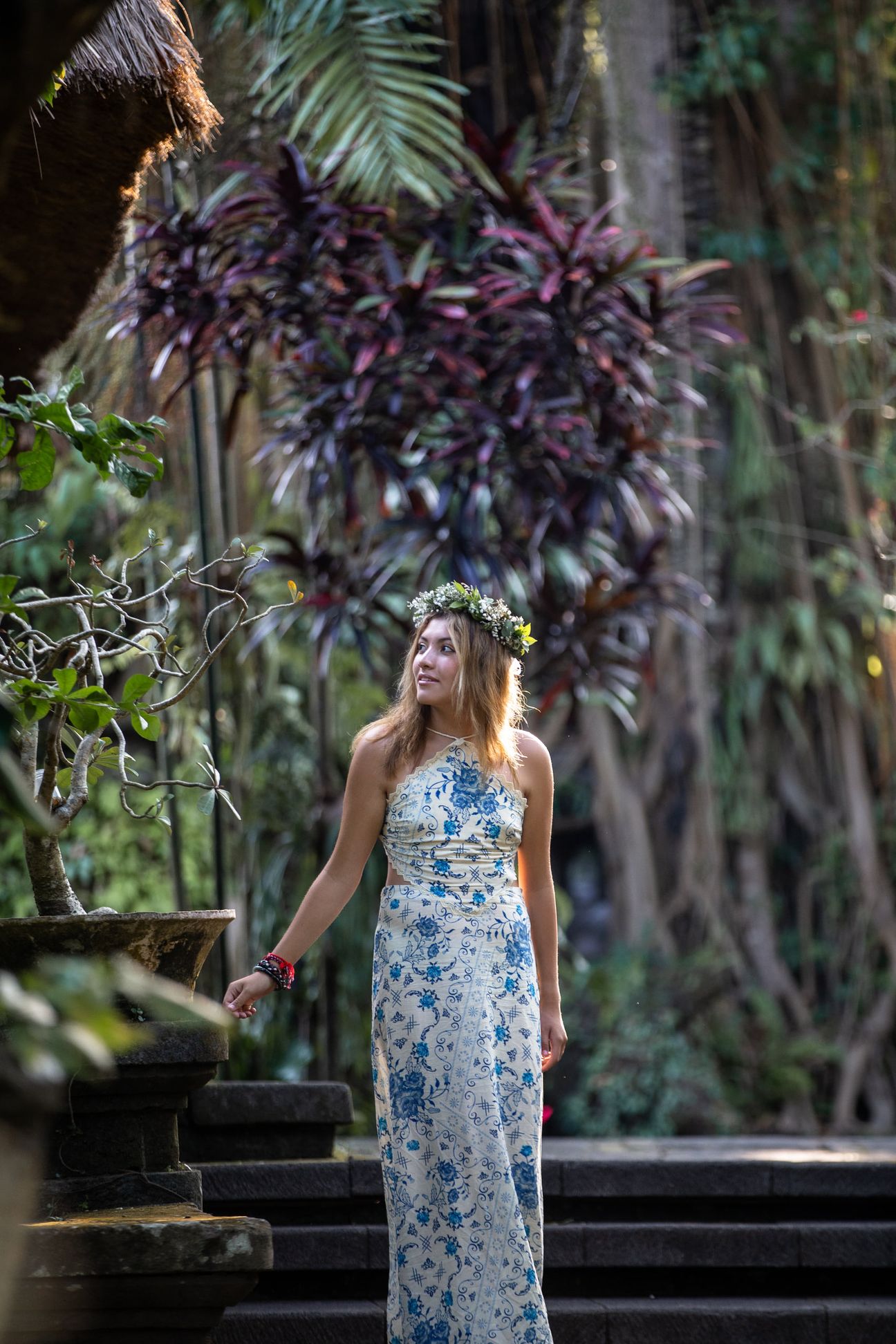 A woman in a floral dress poses in the shade of a tropical Balinese garden