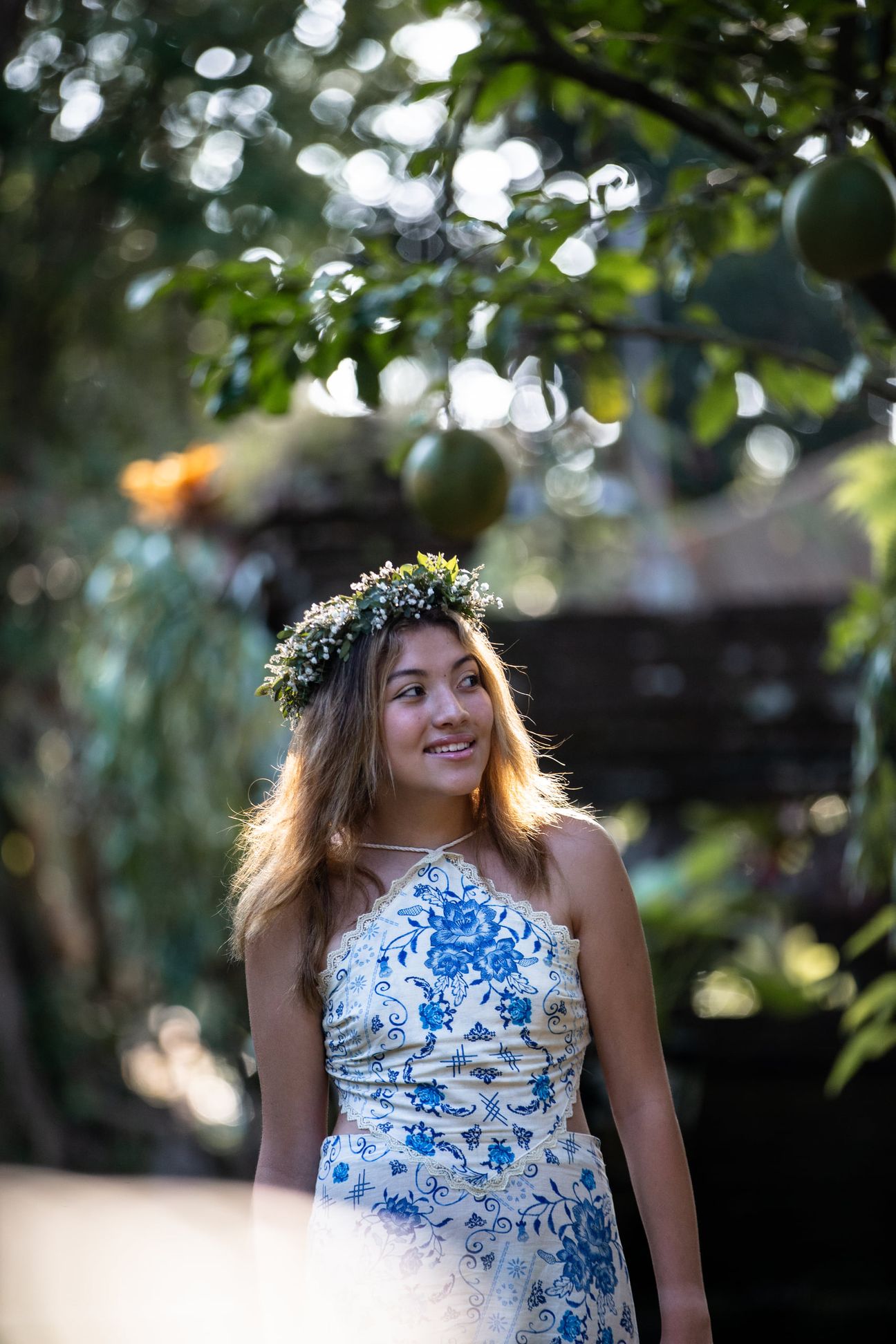 A woman in a floral dress poses in the shade of a tropical Balinese garden